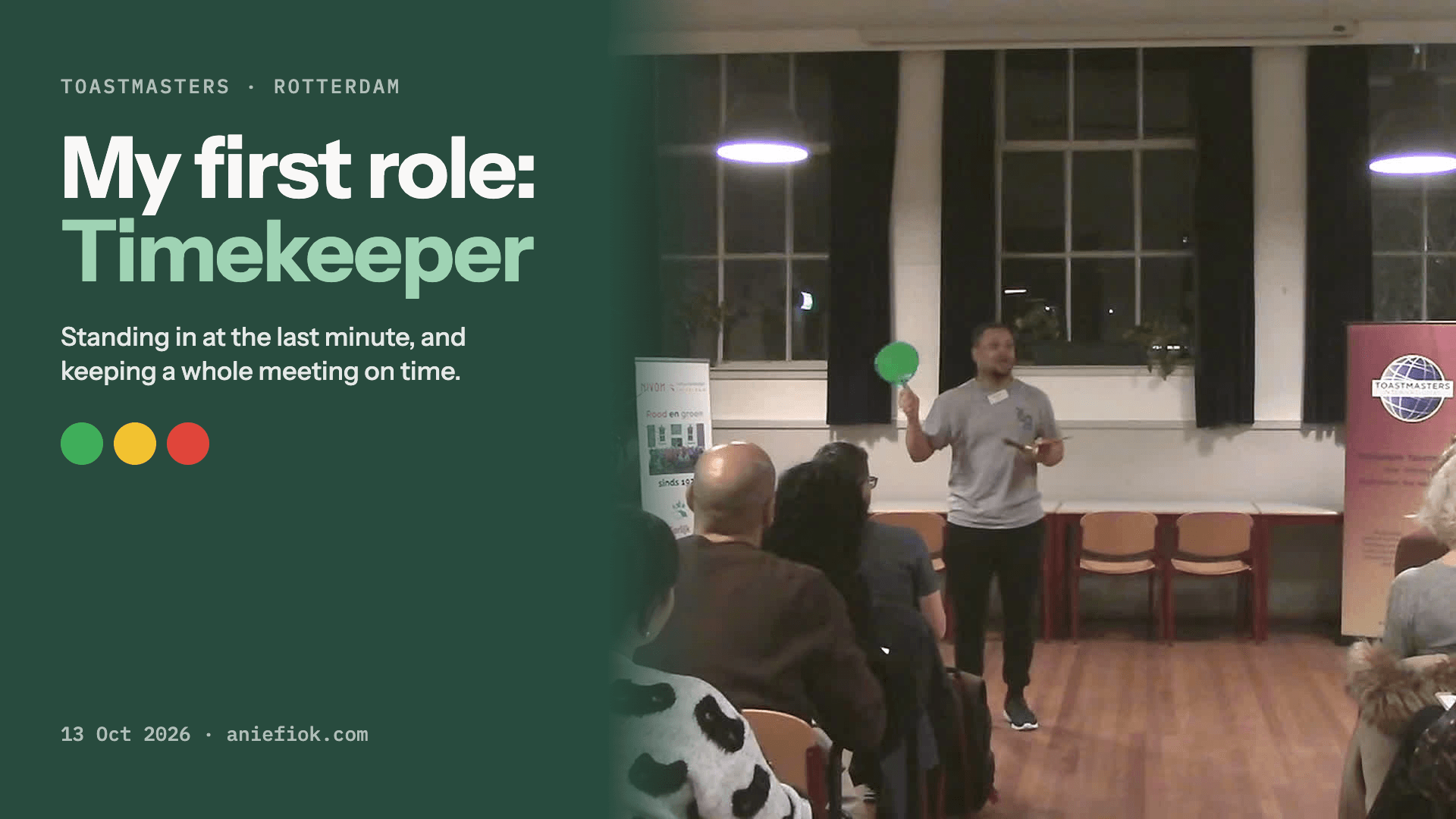 Ani at the front of a Toastmasters meeting room in Rotterdam, raising a green timing card, beside the title: My first role: Timekeeper.