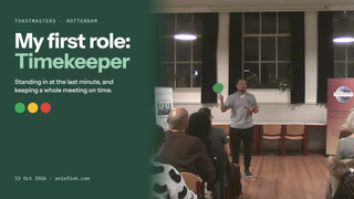 Ani at the front of a Toastmasters meeting room in Rotterdam, raising a green timing card, beside the title: My first role: Timekeeper.